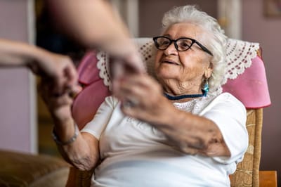Elderly woman smiling while holding hands with a caregiver