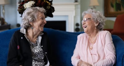 Two elderly women smiling and chatting on a couch