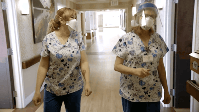 Two staff members wearing masks and scrubs in a hallway
