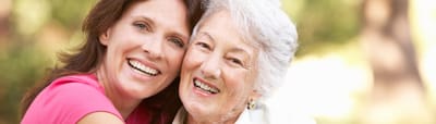 Two women smiling outdoors, embracing each other.