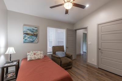 A cozy single resident bedroom with a chair and lamp.