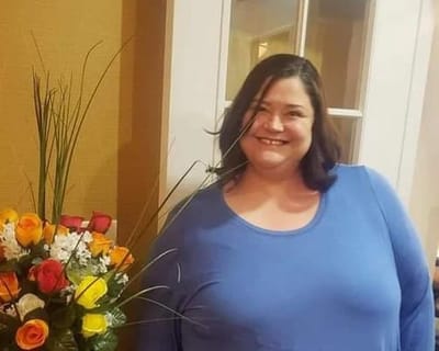 Woman smiling next to a flower arrangement.