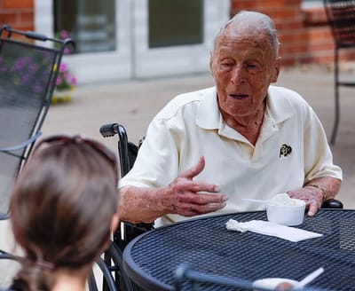 Elderly man enjoying ice cream outdoors with a caregiver