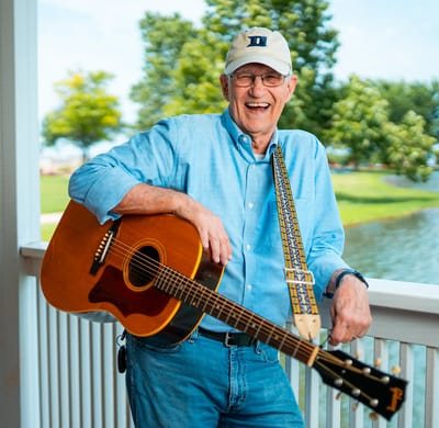 A resident playing guitar outdoors by a pond