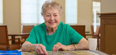 An elderly woman enjoying a puzzle activity in a common area