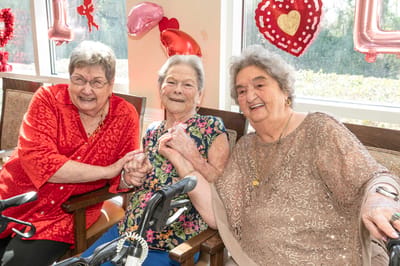 Three elderly residents smiling and holding hands in a decorated room