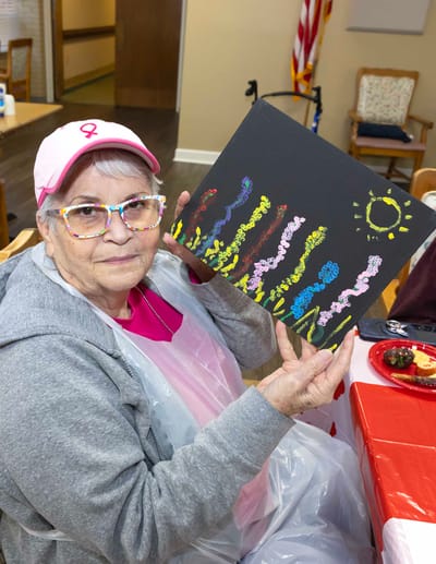 A resident proudly displaying her painting in an activity room