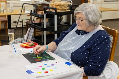 Resident painting at a table with snacks and drinks