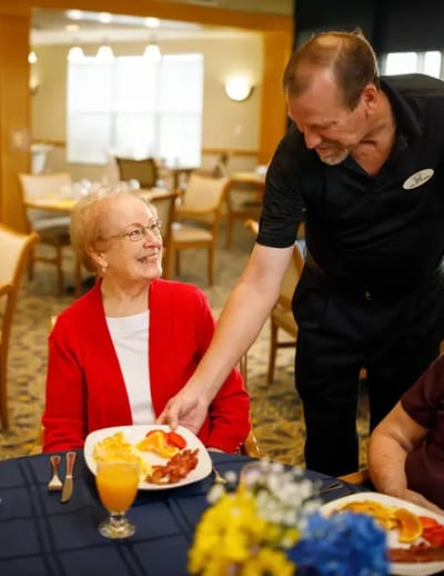 A staff member serving food to a smiling resident