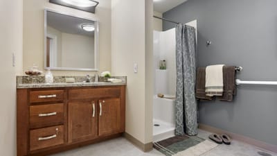 Bridges® by EPOCH at Nashua, memory care in Nashua, NH — Modern bathroom with sink, shower, and storage facilities