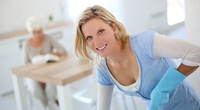 Caregiver cleaning in a bright room with a resident reading