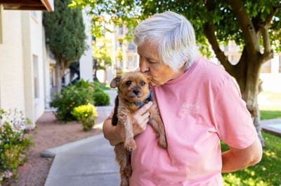 An elderly resident cuddling a small dog outdoors