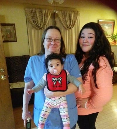 A staff member holding a baby with a young girl