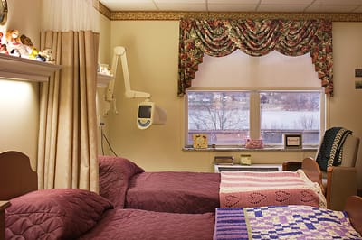 A cozy resident room with two beds and decorative window treatments