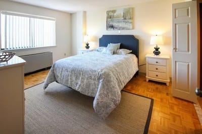 Bright, well-furnished resident room with a bed and lamps