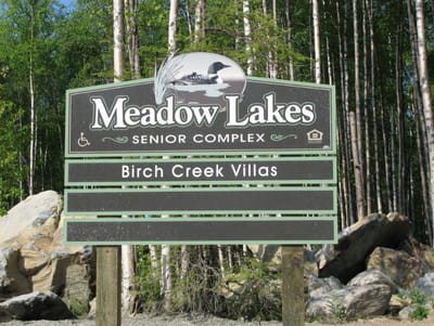 Sign for Meadow Lakes Senior Complex surrounded by trees