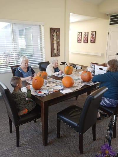 Elderly residents and a child painting pumpkins at a table