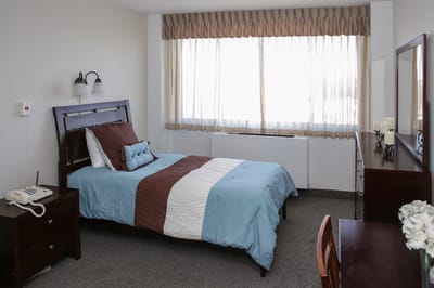 A neatly arranged private resident room with a bed and window