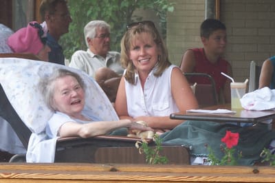 A woman smiling with a resident in a care facility.