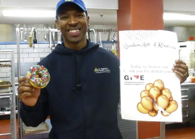 Staff member holding a decorated donut and thank you sign.