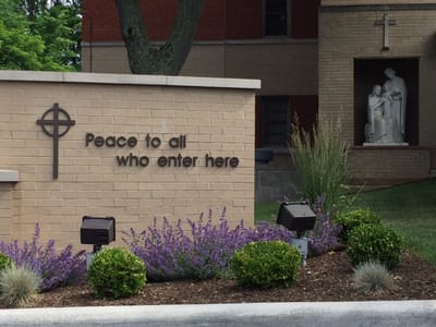 Entrance sign with welcoming message and landscaping.