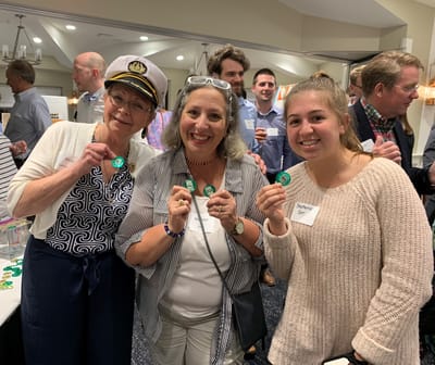 Three women holding celebration pins at an event