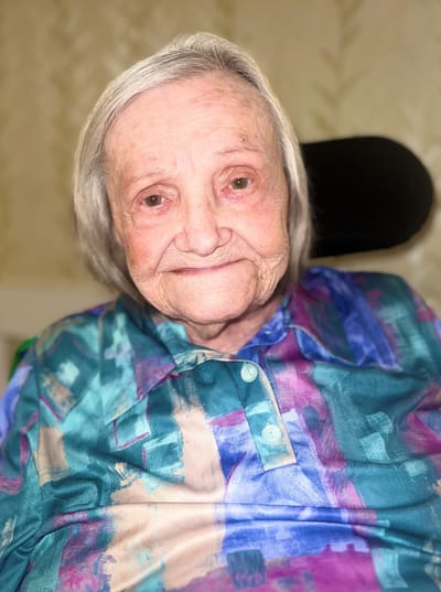 Elderly woman smiling warmly in colorful shirt.