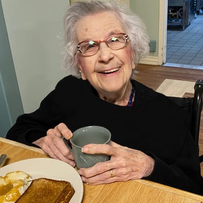 Elderly woman smiling with a drink near her food.