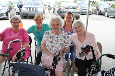 Residents smiling with staff outdoors at the facility.