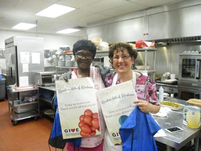 Two staff members holding appreciation signs in the kitchen.