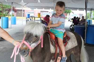 Child riding a pony at an outdoor event.