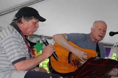 Two men singing and playing guitar at an event.