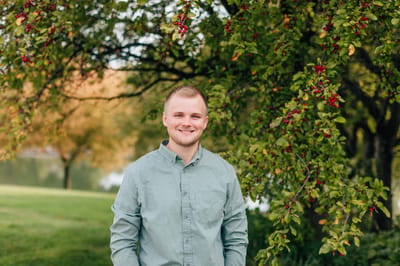 A young man smiling in front of a tree