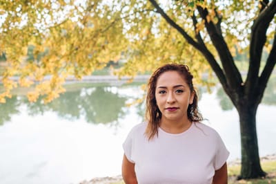 A woman standing near the water under a tree