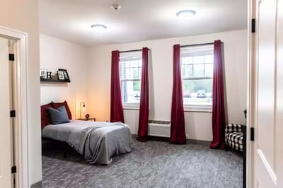 A neatly arranged resident room with a bed and curtains