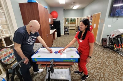 Resident playing air hockey with staff assistance