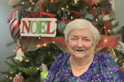 Resident smiling in front of a decorated Christmas tree