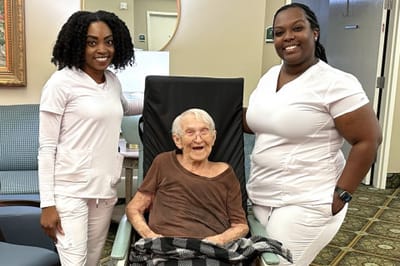Two staff members with a smiling resident in a common area