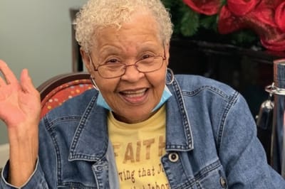Resident smiling and waving in a cozy common area