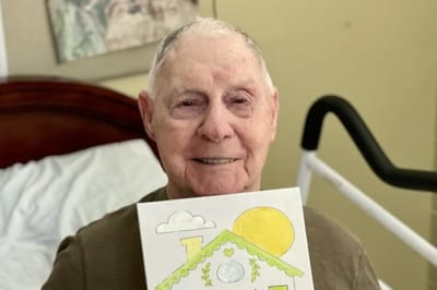 Resident holding up a colorful drawing in their room