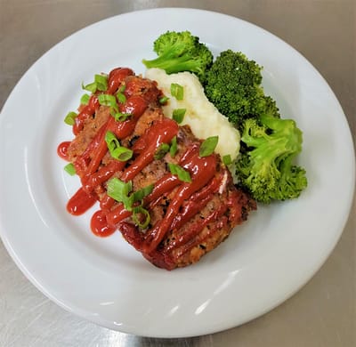 A plated meal featuring meatloaf, broccoli, and mashed potatoes