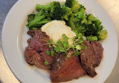 A plate of beef with broccoli and mashed potatoes