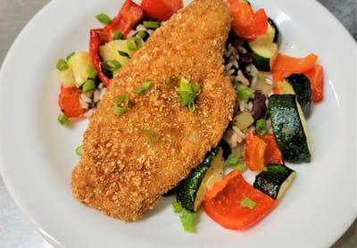 A serving of breaded fish with colorful vegetables