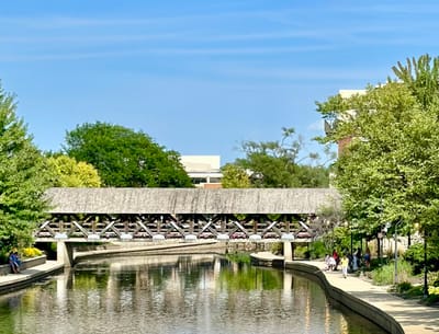 A scenic view of a covered bridge by a tranquil waterway