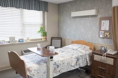 Brightly furnished resident room with bedside table and window