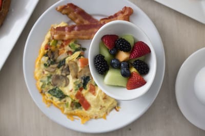 A plate of breakfast with an omelette, bacon, and fruit