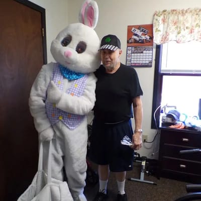 A resident posing with a costumed bunny in a room