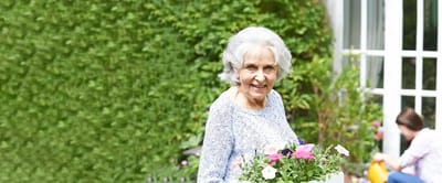 Elderly woman holding a pot of flowers in a garden