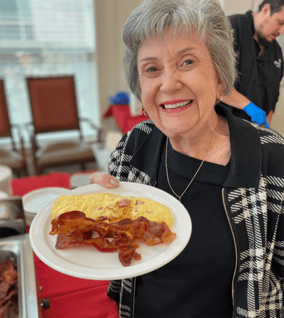 Resident smiling and holding a plate of bacon and omelet