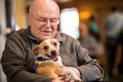 An elderly man holding a happy dog in a cozy common area